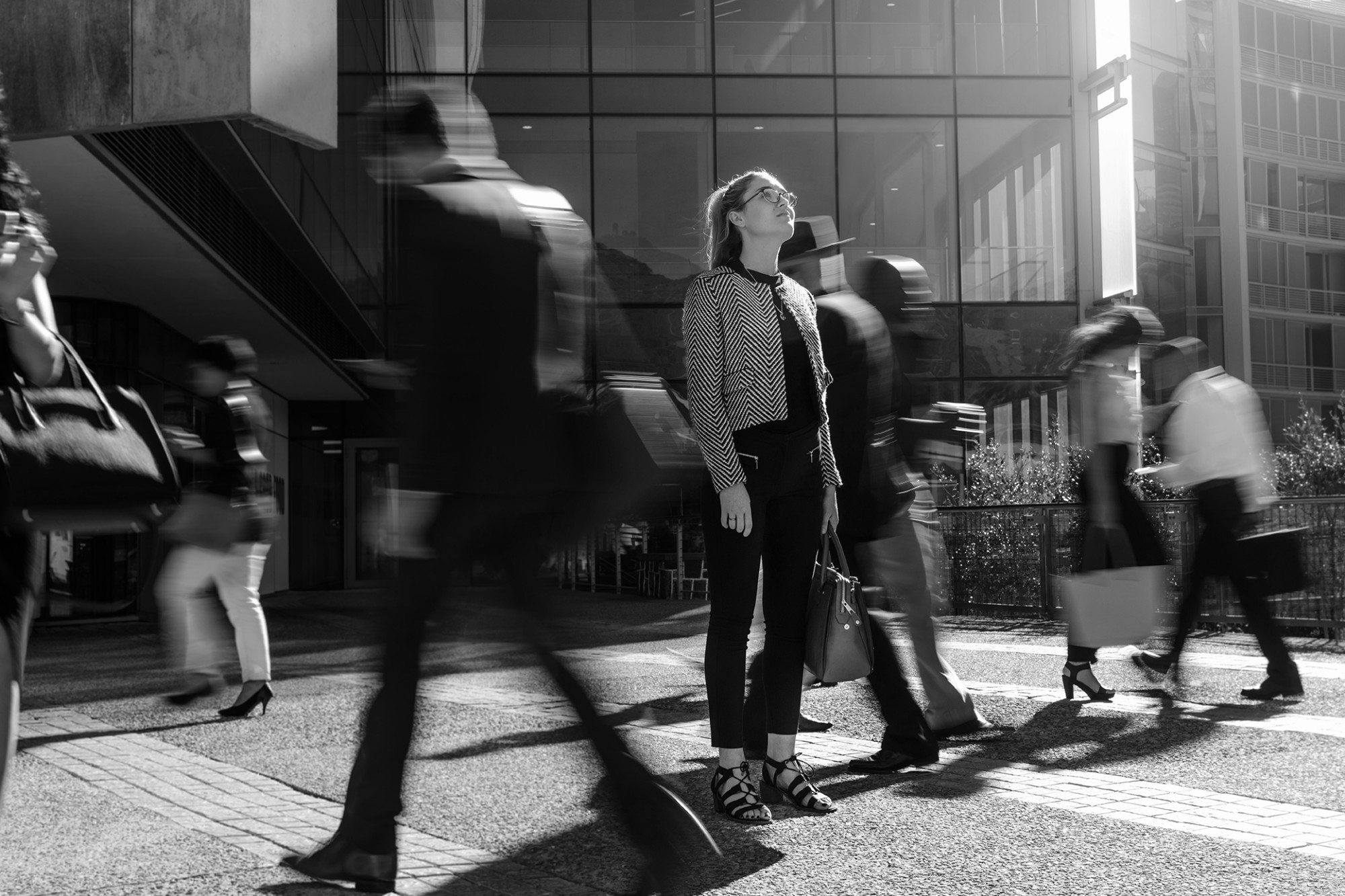 black and white image of a women standing in the streets looking up as people walk around her.